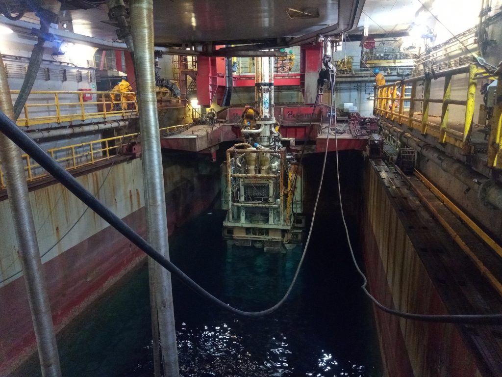 A Picture of a subsea BOP being lowered into the water from the moonpool area of an offshore oil rig